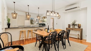 A modern kitchen with white cabinets, a wooden dining table, and black chairs. There are hanging lights and a clock on the wall. - Central Queenstown 3 Bed Villa (Queenstown)