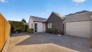 A residential property with a gravel driveway, a detached garage, and a small house with a sloped roof. - Central Queenstown 3 Bed Villa (Queenstown)