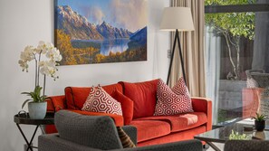 A living room with a red sofa, patterned pillows, a potted plant, and a painting of a mountain landscape. - Central Queenstown 3 Bed Villa (Queenstown)
