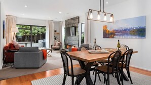 A modern dining area with a wooden table and black chairs, a fireplace, and a large window overlooking a garden. - Central Queenstown 3 Bed Villa (Queenstown)