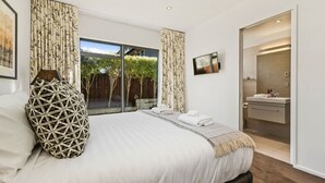 A modern bedroom with a large bed, a flat-screen TV, and a bathroom with a sink and mirror. - Central Queenstown 3 Bed Villa (Queenstown)