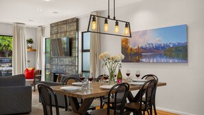 A dining area with a wooden table set for six, surrounded by wicker chairs. A fireplace with a stone facade is visible in the background. - Central Queenstown 3 Bed Villa (Queenstown)