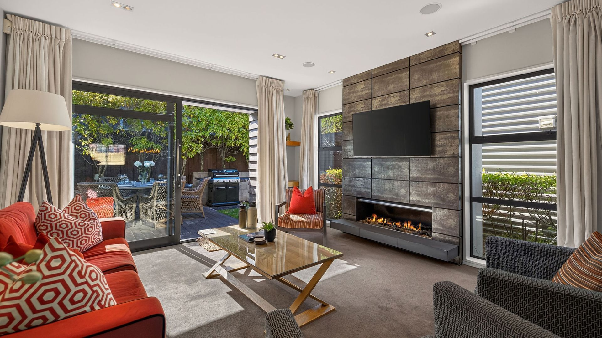 A modern living room with a fireplace, a flat-screen TV, and a dining area with outdoor seating.