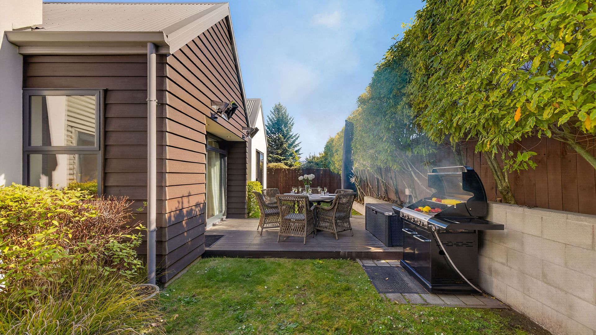 A modern house with a patio, a grill, and a dining area with wicker furniture.