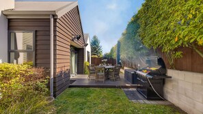 A modern house with a patio, a grill, and a dining area with wicker furniture. - Central Queenstown 3 Bed Villa (Queenstown)