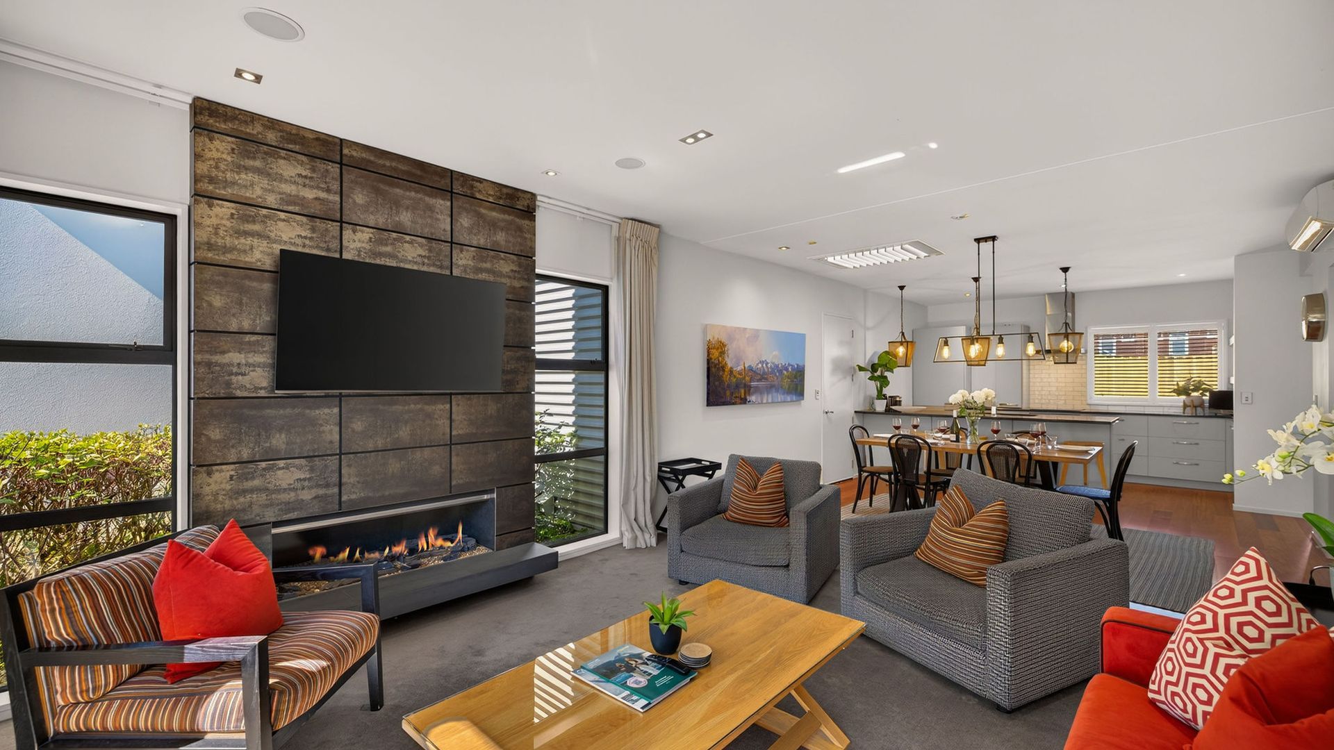 A modern living room with a fireplace, sofas, a coffee table, and a dining area with a kitchen in the background.