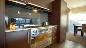 Een moderne keuken met een gasfornuis, oven en uitzicht op bergen door grote ramen.