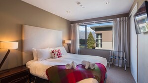 Een hotelkamer met een groot bed, een bureau met een lamp, een aan de muur bevestigde televisie en een raam met uitzicht op de bergen.