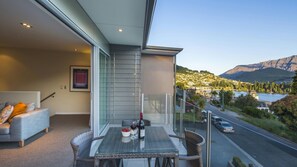 A balcony with a glass table set for two, overlooking a road and a mountainous landscape. - LakeRidge Queenstown Front Row (Queenstown)