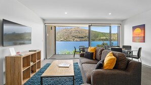 Uma sala de estar moderna com uma grande janela que oferece uma vista panorâmica de um lago e montanhas.
