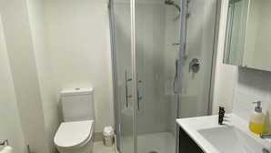 Une salle de bain moderne équipée de toilettes, d’une douche à parois de verre et d’un lavabo avec un miroir au-dessus.