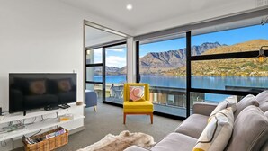 Un salon moderne doté d’un grand téléviseur, de sièges confortables et offrant une vue pittoresque sur un lac.