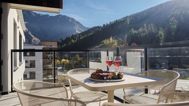 A terrace with a table set for two, featuring a bottle of red wine and a plate of food. - Alpine View Penthouse (Queenstown)