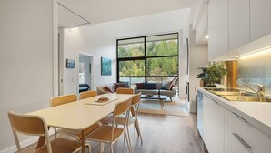 A modern kitchen with a large window, a dining area with a table and chairs, and a living area with a sofa and a coffee table. - Alpine View Penthouse (Queenstown)