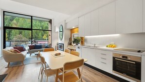 A modern kitchen with white cabinets, a Bosch oven, and a dining area with a wooden table and chairs. - Alpine View Penthouse (Queenstown)