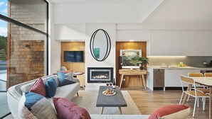 A modern living room with a fireplace, a dining area, and a kitchen. - Alpine View Penthouse (Queenstown)