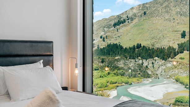 Una camera da letto con un'ampia finestra che si affaccia su un paesaggio montuoso e un fiume.