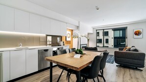 Una cucina moderna con mobili bianchi, un tavolo da pranzo in legno e sedie nere. Si vede un'ampia finestra con vista sugli edifici.