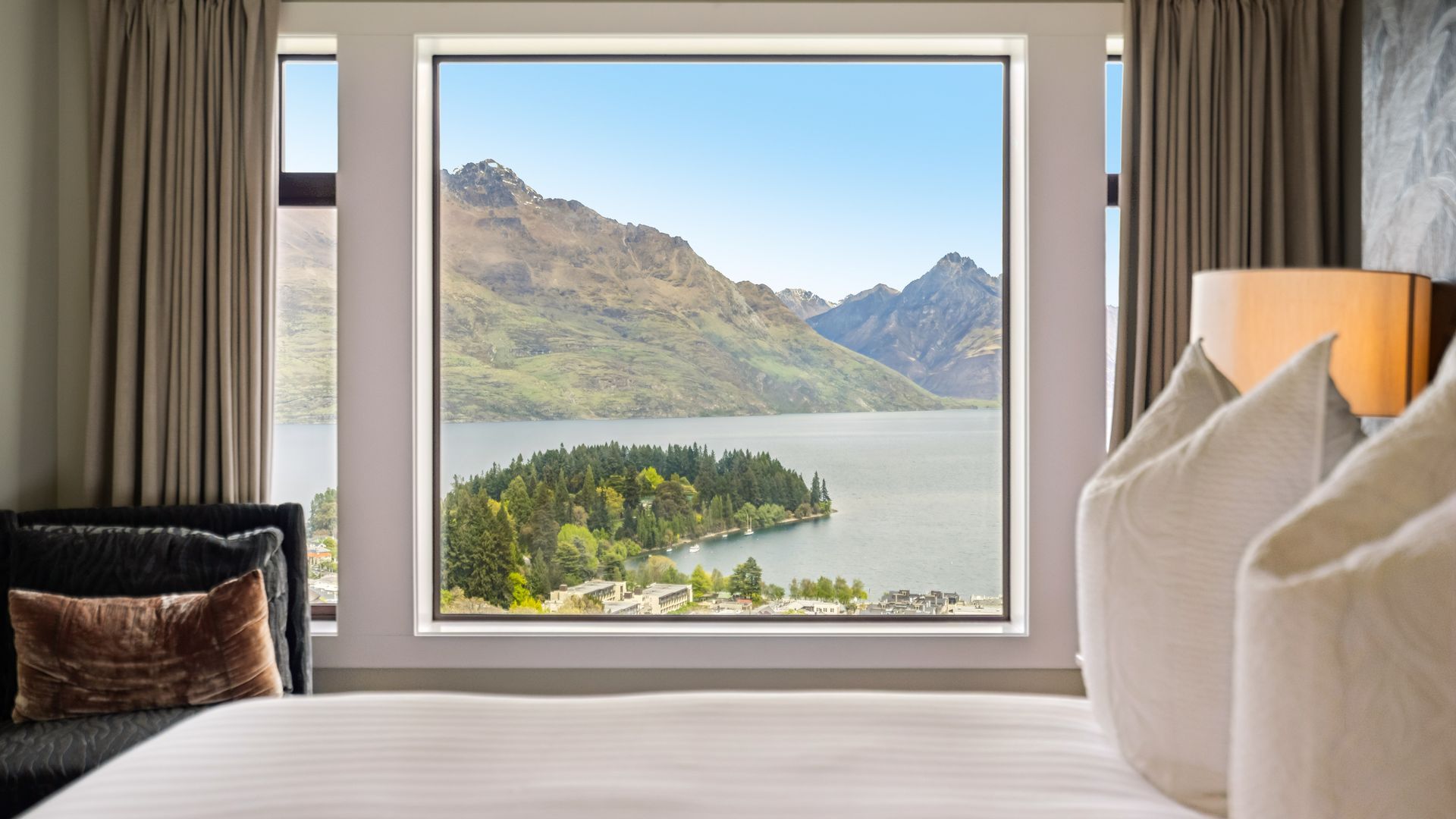 A hotel room with a large window offering a view of a lake and mountains.
