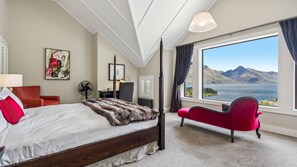 Ein Schlafzimmer mit einem großen Bett, einem roten Sessel, einem Ventilator und Blick auf einen See und Berge.