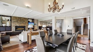 A spacious living area with a fireplace, a dining table with chairs, and a kitchen in the background. - Commonage Grand Villa 2 Bedroom (Queenstown)