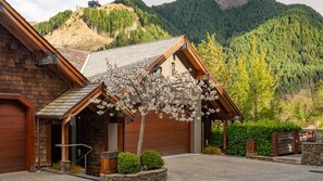Une cabane en bois avec un toit en pente, entourée d’un jardin bien entretenu et dominant un paysage montagneux.