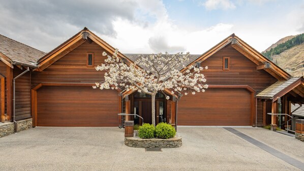 A wooden building with a central entrance and two side wings, surrounded by a gravel driveway and a stone border. - Commonage Grand Villa 2 Bedroom (Queenstown)