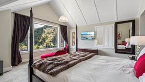 A bedroom with a four-poster bed, a large window with curtains, a red chair, a flat-screen TV, and a mirror. - Commonage Grand Villa 2 Bedroom (Queenstown)