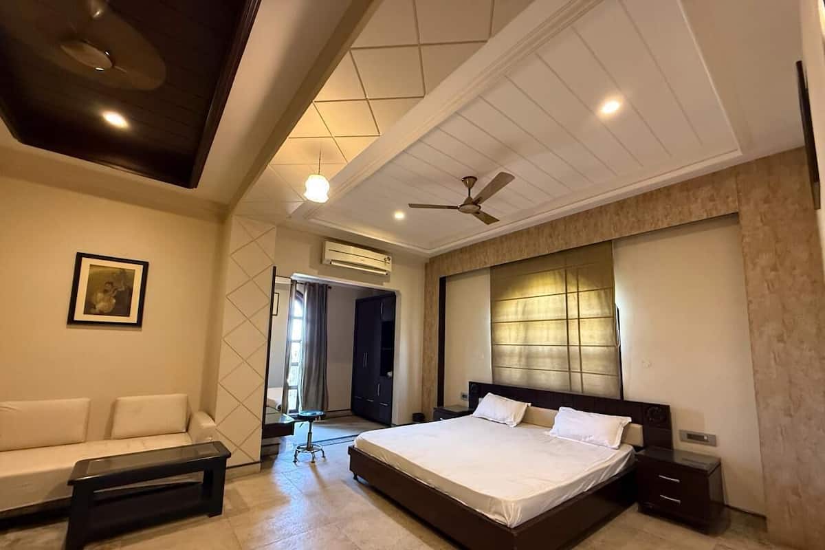 A modern bedroom with a large bed, a sofa, a ceiling fan, and an air conditioning unit.