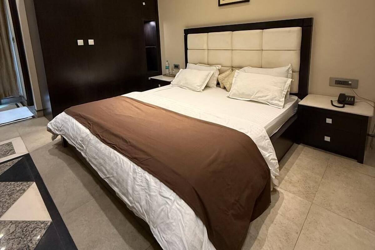 A modern bedroom with a large bed, a dark wardrobe, a bedside table, and a ceiling with recessed lighting.