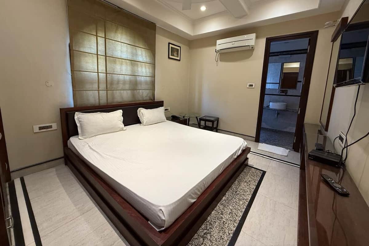 A modern bedroom with a large bed, a ceiling fan, an air conditioning unit, and a television.