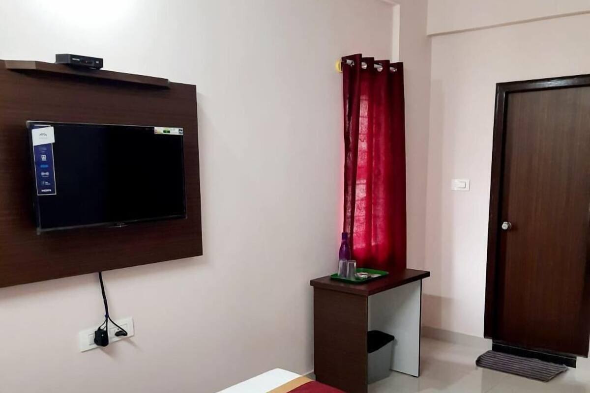 A hotel room with a bed, a desk, a TV mounted on the wall, and a wardrobe.