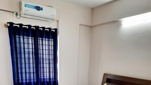 A neatly made bed with white linens and a red and yellow bed runner, a blue curtain, and a small blue rug on a tiled floor. - Hotel Royal Suites (Bengaluru)
