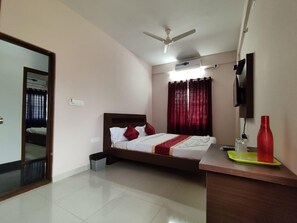 A bedroom with a bed, a desk, a mirror, a ceiling fan, and a TV. - Hotel Royal Suites (Bengaluru)