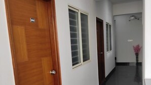 A hallway with a wooden door marked '202', a window, and a vase with pink flowers. - Hotel Royal Suites (Bengaluru)