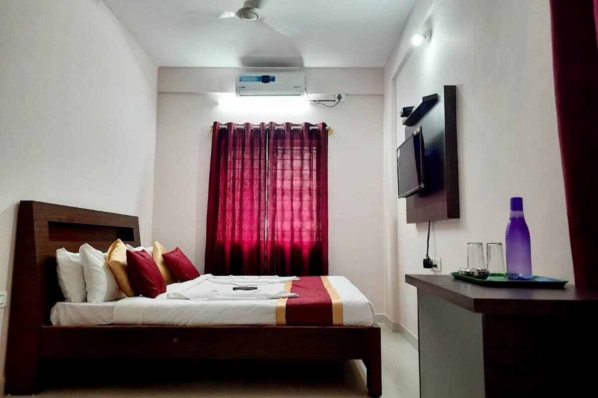 A hotel room with a bed, a TV mounted on the wall, and a ceiling fan.
