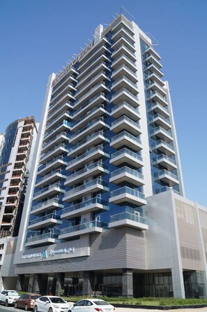 A modern high-rise building with multiple balconies and a prominent signage at the base. - Chic studio located in the heart of Business Bay (buisness bay)