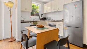 Une cuisine compacte avec des meubles blancs, un réfrigérateur en acier inoxydable, un four à micro-ondes et une table à manger avec des chaises.