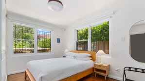 Une chambre à coucher avec un lit en bois, deux tables de chevet, une lampe et une grande fenêtre donnant sur un paysage verdoyant.