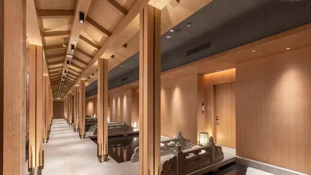 Un pasillo moderno de hotel con paneles de madera, suelo reflectante y una fuente central.