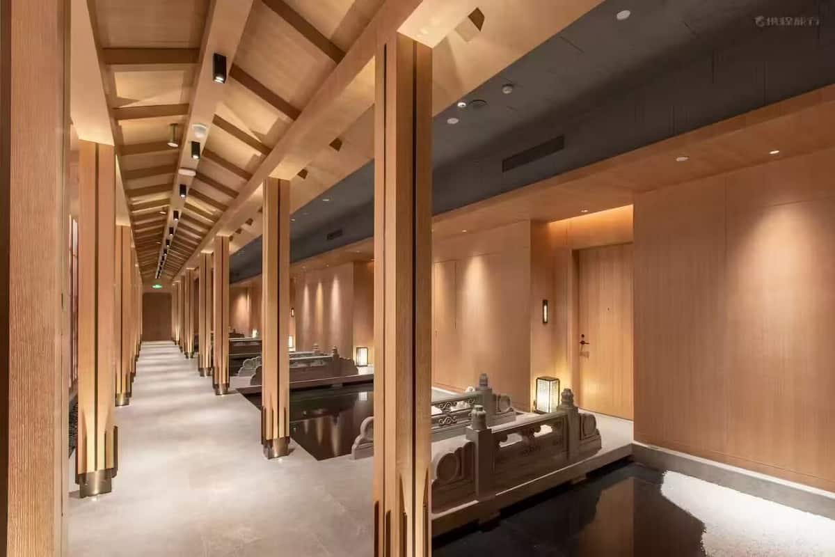 Un pasillo moderno de hotel con paneles de madera, suelo reflectante y una fuente central.