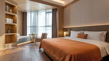 Quarto de hotel moderno com uma cama grande, área de estar com mesa e cadeiras, e prateleiras embutidas decoradas com objetos.