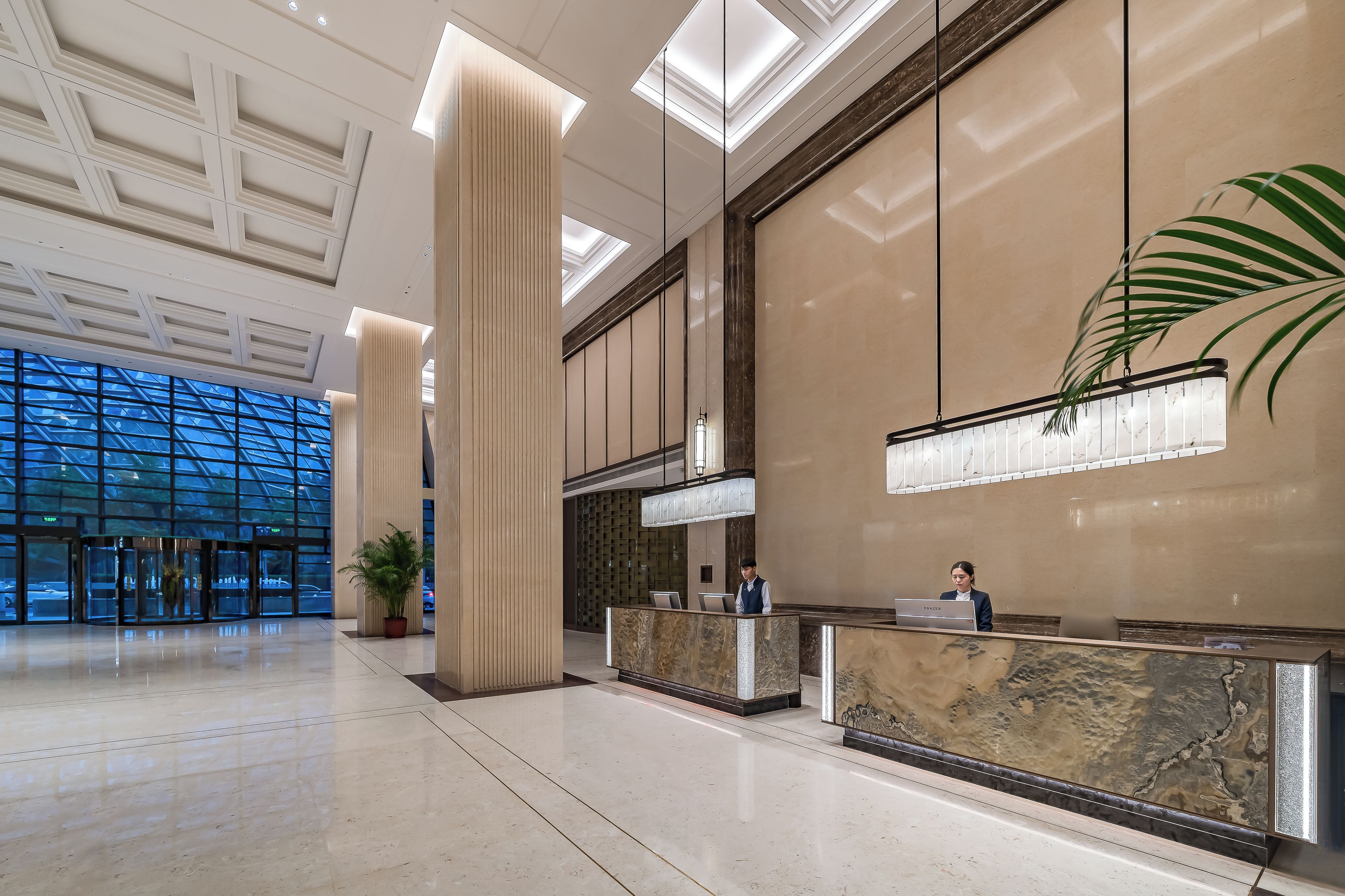 A spacious lobby with high ceilings, a reception desk, and a large window offering a view of the outside.