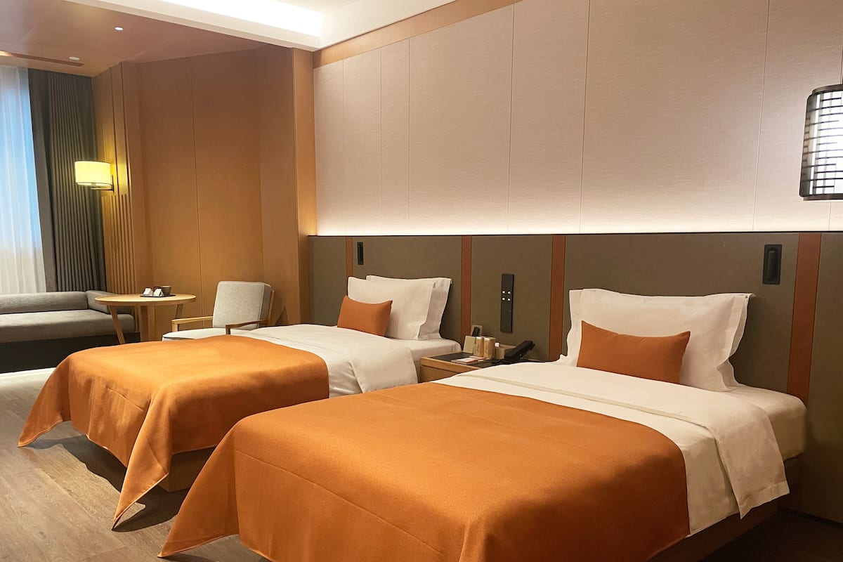 Una habitación de hotel con dos camas, un sofá, una mesita y una lámpara.