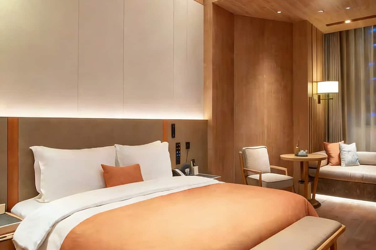 Una habitación de hotel moderna con una cama grande, mesitas de noche, una zona de estar con sofá y sillones, y una pequeña mesa.