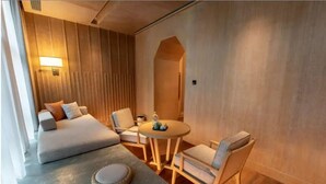 Una habitación de hotel moderna con una cama, una mesita redonda pequeña, dos sillas y una lámpara fijada a la pared.