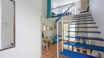 A staircase with blue steps leading to a second-floor area, a dining table with chairs, and a bed with blue bedding.