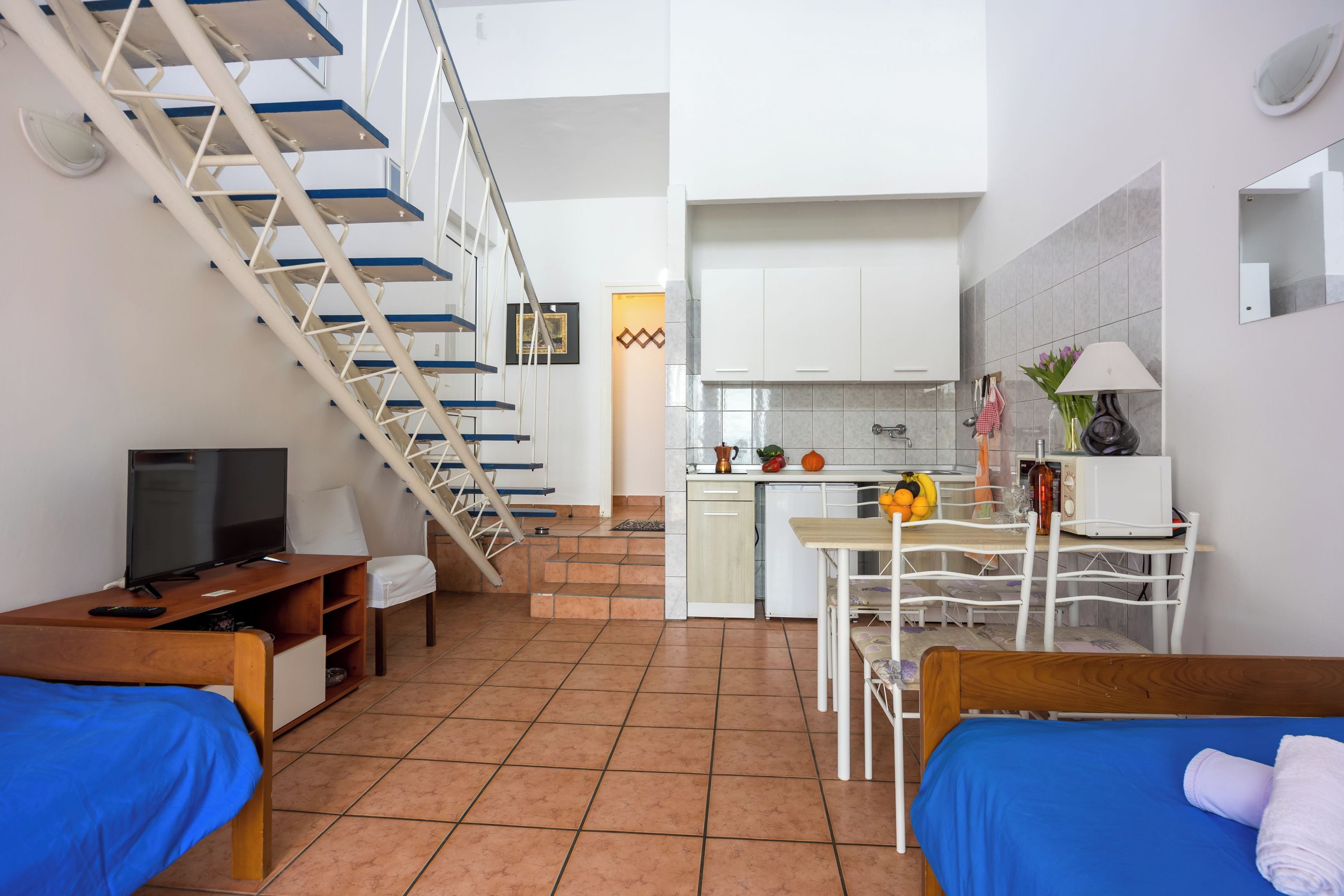 Un espace de vie compact comprenant un escalier, un coin cuisine, un espace repas et un lit.