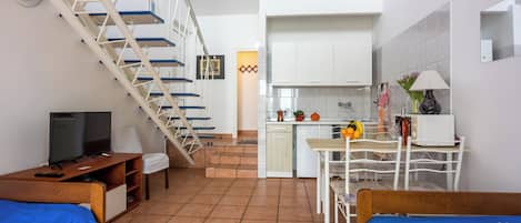 Un espacio habitable compacto con escaleras, kitchenette, zona de comedor y cama.