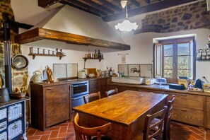A rustic kitchen with wooden cabinets, a large wooden table, and a stone wall.